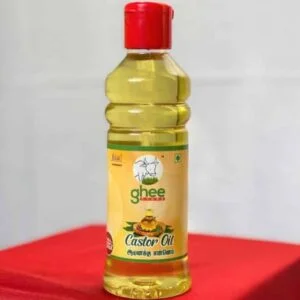 A bottle of castor oil with a red cap, featuring a label that reads "ghee" and "Castor Oil" in Tamil, placed on a red surface.