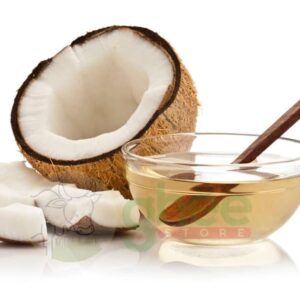 A halved coconut showing its white flesh, with pieces of coconut next to it, and a glass bowl of oil with a wooden spoon.