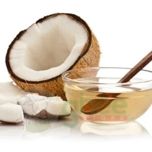 A halved coconut showing its white flesh, with pieces of coconut next to it, and a glass bowl of oil with a wooden spoon.