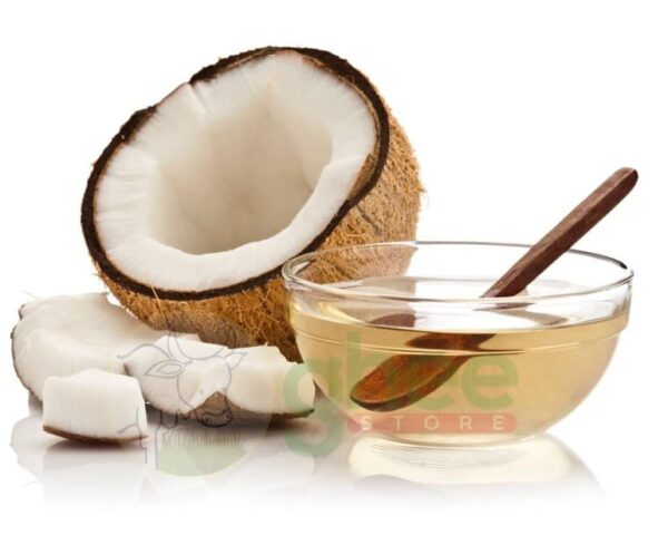 A halved coconut showing its white flesh, with pieces of coconut next to it, and a glass bowl of oil with a wooden spoon.