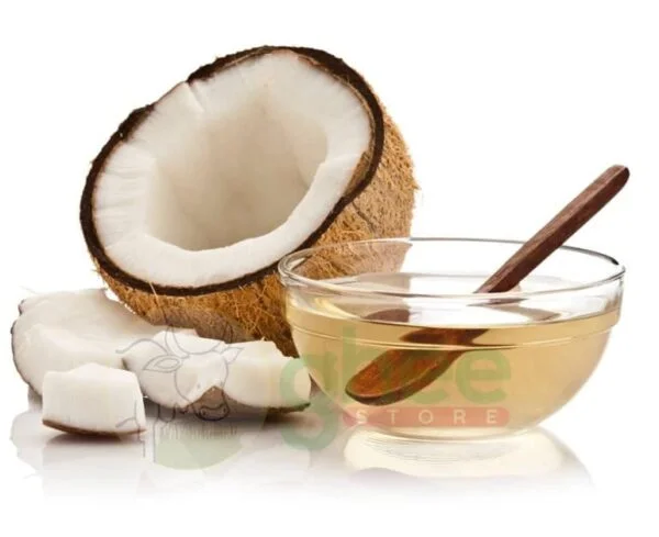 A halved coconut showing its white flesh, with pieces of coconut next to it, and a glass bowl of oil with a wooden spoon.