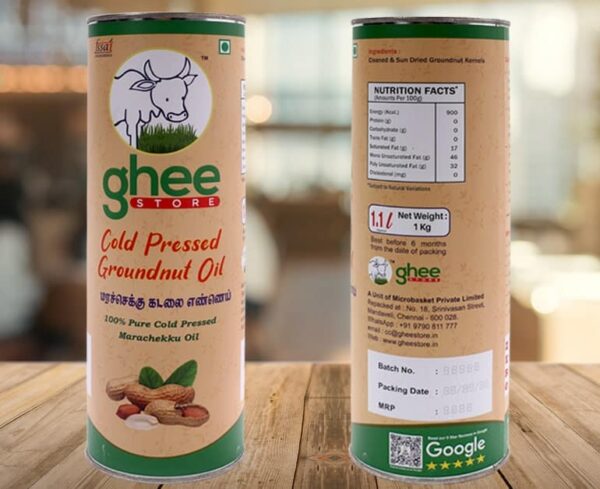 A cylindrical container of cold pressed groundnut oil, labeled "ghee STORE," featuring a cow illustration and text in both English and Tamil. The container includes nutritional facts on one side, with details on the product's weight (1 kg) and packaging information. It showcases a natural, earthy design with peanuts depicted at the bottom.