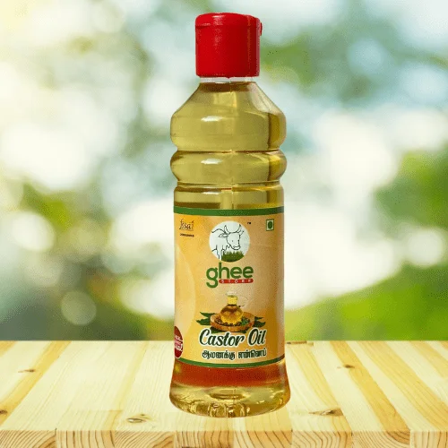 Bottle of castor oil with a red cap, featuring a label with text in English and another script, set on a wooden surface with a blurred green background.