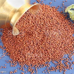 A brass vessel tipped over, spilling small reddish-brown Finger Millet onto a blue surface, with a sprig of green herbs in the corner.