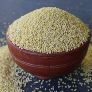 A clay bowl overflowing with yellow millet grains, with some grains scattered around the bowl.